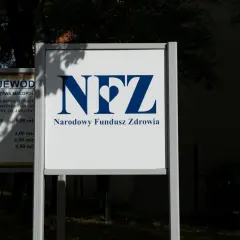 Tablica z logo NFZ i napisem Narodowy Fundusz Zdrowia. Obok tablica z informacjami o inwestycji w szpital.