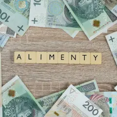 Litery "ALIMENTY" ułożone z kafelków na drewnianym tle, otoczone polskimi banknotami.