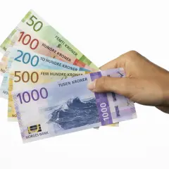 Dłoń trzyma banknoty: 50, 100, 200, 500 i 1000. To korony norweskie, czyli jaka waluta jest w Norwegii.