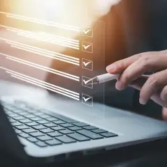 Ręka z długopisem zaznacza punkty na liście kontrolnej na ekranie laptopa. Proces zmiany regulaminu zakładowego funduszu świadczeń socjalnych.