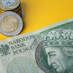 Stos monet i banknotów 100 zł na żółtym tle.