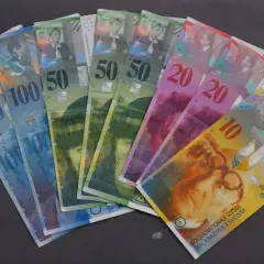 Różne banknoty CHF, czyli franków szwajcarskich, leżą na ciemnym tle. Widać nominały 10, 20, 50 i 100.