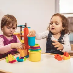 Dwie dziewczynki bawią się klockami przy stoliku. Dofinansowanie do żłobka może pomóc rodzicom w zapewnieniu opieki maluchom.