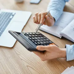 Osoba liczy na kalkulatorze, analizując co składa się na oprocentowanie kredytu. Obok leży laptop i notatnik.