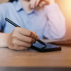 Osoba korzysta ze smartfona i rysika, szukając informacji, jak zmienić numer telefonu w mBank.