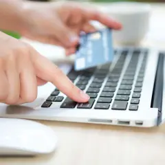Dłoń z kartą płatniczą nad klawiaturą laptopa, przygotowuje się do wykonania przelewu. Sprawdź godziny przelewów PKO, aby zrobić to sprawnie.