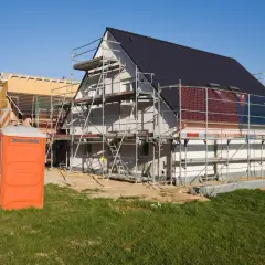 Budowa domu w toku, rusztowania, toaleta przenośna. Dowiedz się, jak założyć firmę budowlaną z dofinansowaniem.