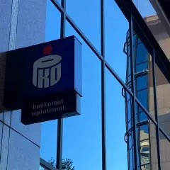Niebieski szyld PKO BP z napisem "bankomat wpłatomat" na tle szarej ściany i błękitnego nieba. To jak eliksir dla Twoich finansów.