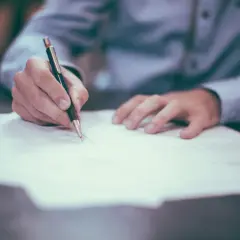 Ręka pisze długopisem na papierze. Proces sprawdzania BIK osoby zmarłej wymaga analizy dokumentów.