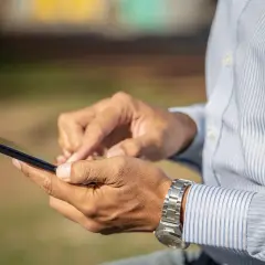 Mężczyzna w koszuli z długim rękawem i zegarkiem na nadgarstku korzysta z telefonu, szukając informacji, jak zamknąć konto Revolut.