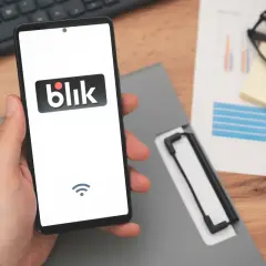 Dłoń trzyma smartfon z logo Blik, sugerując szybki zarobek. Na biurku leżą dokumenty i okulary.