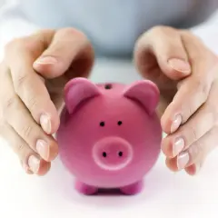 Różowa świnka-skarbonka pod dłońmi. Zastanawiasz się, ile wynosi składka na fundusz pracy?
