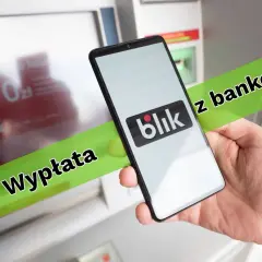 Jak wypłacić pieniądze z bankomatu Blikiem? Smartfon z logo Blik w dłoni przed bankomatem.