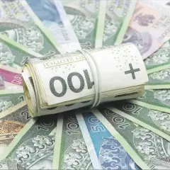 Zwijana paczka banknotów 100 zł, otoczona innymi polskimi banknotami. To symbol bezpieczeństwa finansowego, jak fundusz gwarancyjny chroniący oszczędności.