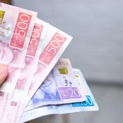 Dłoń trzyma kilka banknotów szwedzkich koron, w tym 500-koronowe.