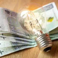 Żarówka na stosie banknotów 100 zł. Zastanawiasz się, jak dostać dofinansowanie do prądu?