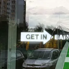 Czy lokaty w Getin Banku są bezpieczne? Znak "GET IN BANK" odbija się w szybie, obok samochodów i budynków.