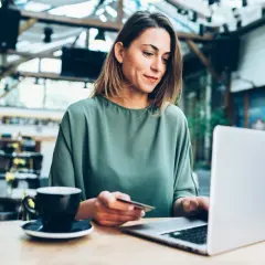 Kobieta z kartą płatniczą przy laptopie, realizuje przelew w banku Pekao.