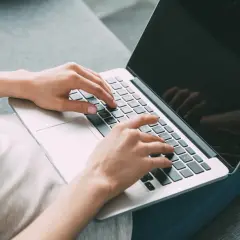 Kobieta pisze na laptopie, szukając informacji, jak zamknąć debet w Millennium.