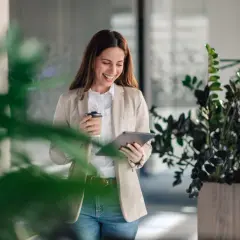 Uśmiechnięta kobieta z kawą i tabletem, zastanawia się, ile można mieć pożyczek w Providencie.