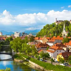 Widok na rzekę Ljubljanicę, most i miasto z zamkiem na wzgórzu w Słowenii.