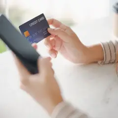 Kobieta używa telefonu i karty kredytowej, być może w celu zwrotu nierozliczonej transakcji Peako.