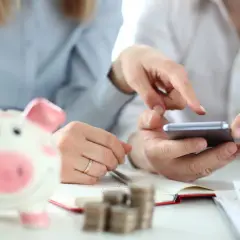 Odkryj, czym jest zakładowy fundusz świadczeń socjalnych. Dwie osoby analizują dane na smartfonie, obok świnka-skarbonka i stos monet.