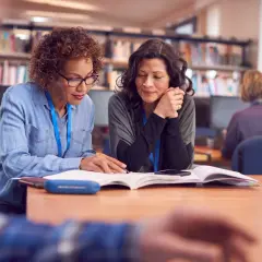 Dwie kobiety studiują w bibliotece, szukając informacji, jak zdobyć dofinansowanie na studia zaoczne.