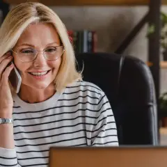 Uśmiechnięta kobieta w okularach rozmawia przez telefon, być może właśnie dowiedziała się, że czy smart pożyczka dzwoni do pracodawcy.