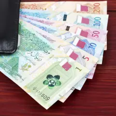 Katar jaka waluta? Na zdjęciu widać stos banknotów katarskich riali, od 1 do 200, częściowo schowanych w czarnym portfelu.