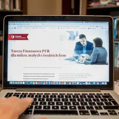 Szukasz informacji, jak sprawdzić czy firma dostała dofinansowanie z tarczy? Na ekranie laptopa wyświetla się strona o Tarczę Finansową PFR dla mikro, małych i średnich firm.