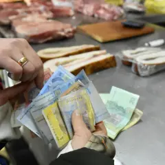 Ręce trzymają stos banknotów. Widać napisy "Національний банк України". To ukraińska waluta, hrywna, używana do zakupu mięsa na targu.