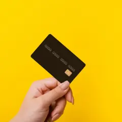 Dłoń trzyma czarną kartę z widocznym chipem i numerem. Idealna do płatności online i w sklepach.