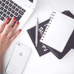 Kobieta pisze na laptopie, obok leży telefon, notatnik i długopis. Zastanawia się, ile kosztuje przelew natychmiastowy.