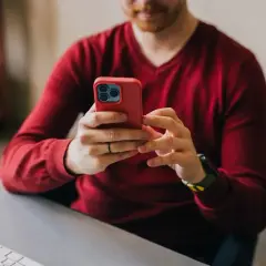 Mężczyzna w czerwonym swetrze korzysta z telefonu, szukając informacji, jak zrobić przelew ekspresowy mBank.