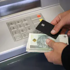 Ręce trzymające banknoty i kartę zbliżają się do bankomatu, pokazując, jak wpłacić pieniądze na konto.