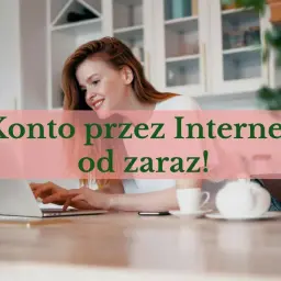 Uśmiechnięta kobieta z rudymi włosami pracuje na laptopie, zakładając konto online. Na stole stoi filiżanka i czajniczek.
