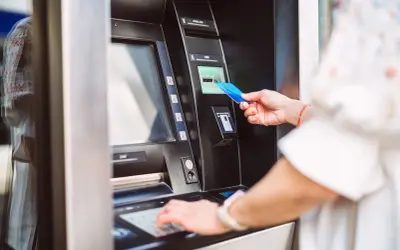Kobieta wkłada kartę do bankomatu Alior Bank. Korzystaj z bankomatów bez prowizji.