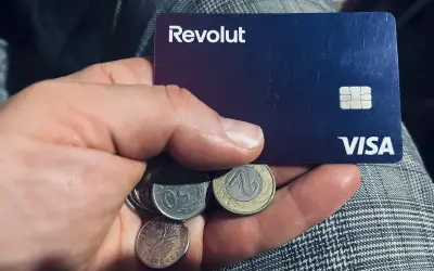 Dłoń trzyma kartę Revolut i polskie monety. Kto jest właścicielem Revolut? To pytanie, na które odpowiedź znajdziesz w aplikacji.