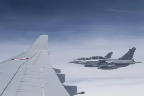 Dwa myśliwce Rafale, napędzane silnikami Safran, lecą w formacji nad chmurami. Widoczny fragment skrzydła samolotu z francuską kokardą.