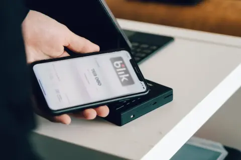 Dłoń trzyma smartfon z aplikacją Blik. Dowiedz się, jak zmienić limit Blik w Millenium, by bezpiecznie zarządzać finansami.