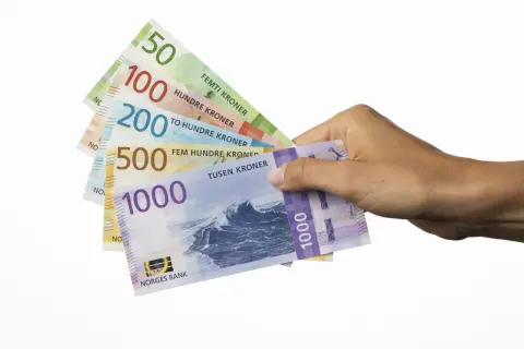 Dłoń trzyma banknoty: 50, 100, 200, 500 i 1000. To korony norweskie, czyli jaka waluta jest w Norwegii.