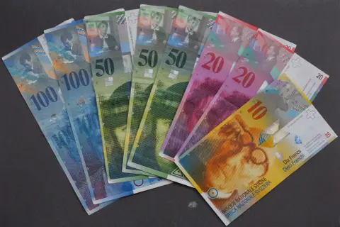 Różne banknoty CHF, czyli franków szwajcarskich, leżą na ciemnym tle. Widać nominały 10, 20, 50 i 100.