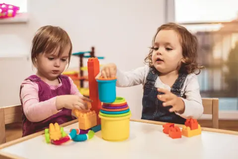 Dwie dziewczynki bawią się klockami przy stoliku. Dofinansowanie do żłobka może pomóc rodzicom w zapewnieniu opieki maluchom.