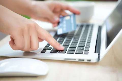 Dłoń z kartą płatniczą nad klawiaturą laptopa, przygotowuje się do wykonania przelewu. Sprawdź godziny przelewów PKO, aby zrobić to sprawnie.