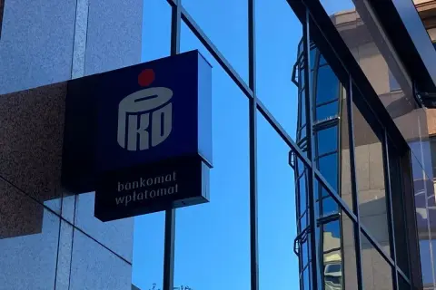 Niebieski szyld PKO BP z napisem "bankomat wpłatomat" na tle szarej ściany i błękitnego nieba. To jak eliksir dla Twoich finansów.
