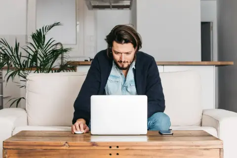 Mężczyzna siedzi na kanapie, pracując na laptopie. Wpisuje swój adres rozliczeniowy, aby dokończyć zamówienie.