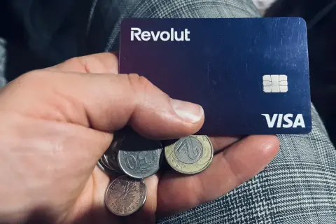 Dłoń trzyma kartę Revolut i polskie monety. Kto jest właścicielem Revolut? To pytanie, na które odpowiedź znajdziesz w aplikacji.