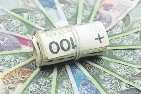 Zwijana paczka banknotów 100 zł, otoczona innymi polskimi banknotami. To symbol bezpieczeństwa finansowego, jak fundusz gwarancyjny chroniący oszczędności.