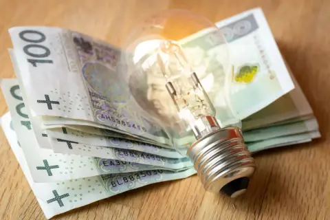 Żarówka na stosie banknotów 100 zł. Zastanawiasz się, jak dostać dofinansowanie do prądu?
